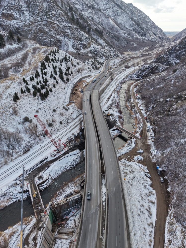 Mountain road winding through a snowy valley with trains running parallel