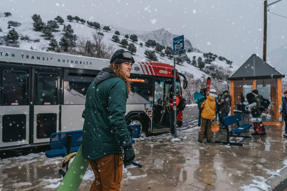 Snowy bus stop with snowboarders and skiers waiting to board the parked UTA bus.